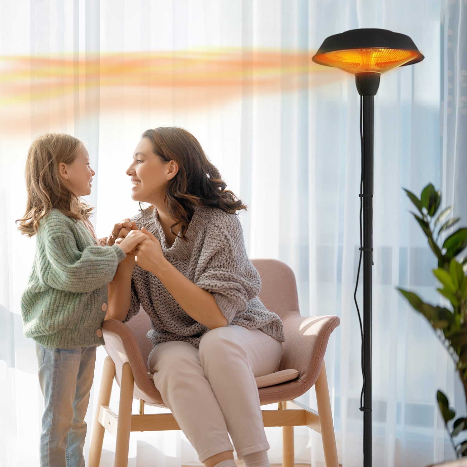 Mother with her daughter sitting on chair beside an electric heater